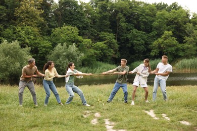 Photo of Team building. Group of happy people playing tug of war with rope outdoors