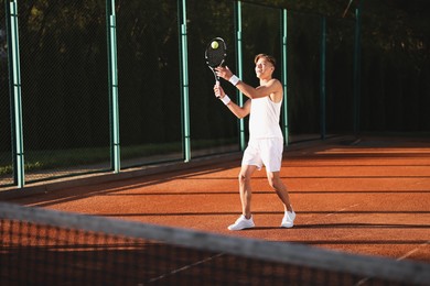 Photo of Young man playing tennis at court on sunny day. Space for text
