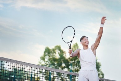 Photo of Young man playing tennis at court on sunny day, low angle view. Space for text