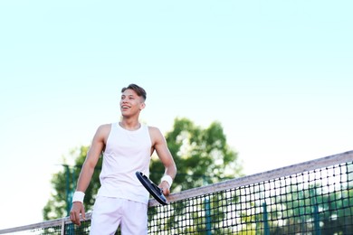 Photo of Young man playing tennis at court on sunny day, low angle view. Space for text