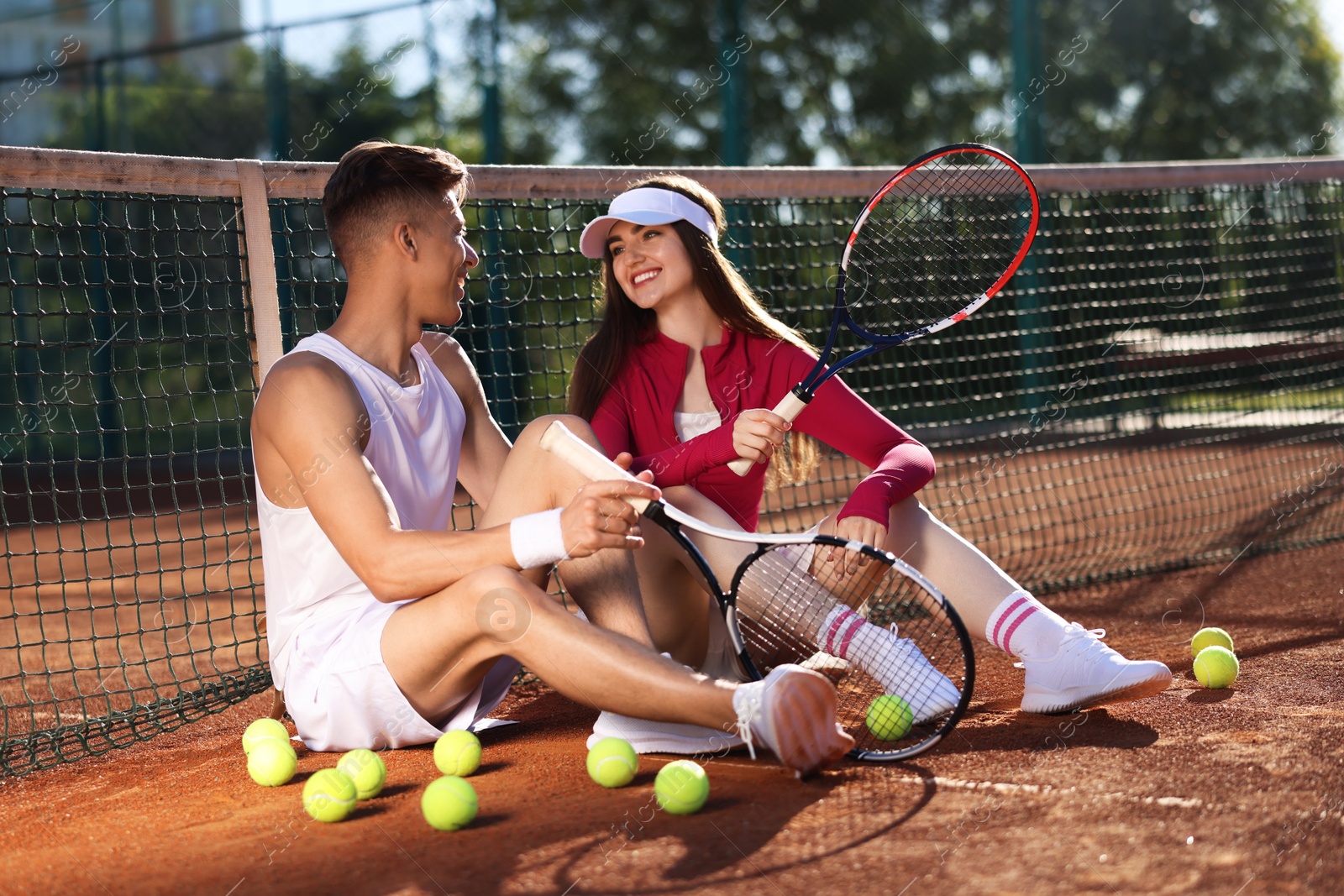 Happy couple with rackets and balls at tennis court Photo of Happy couple with rackets and balls at tennis court