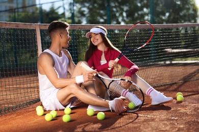 Photo of Happy couple with rackets and balls at tennis court