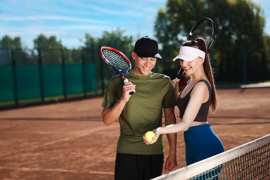 Photo of Happy couple with rackets and ball at tennis court. Space for text