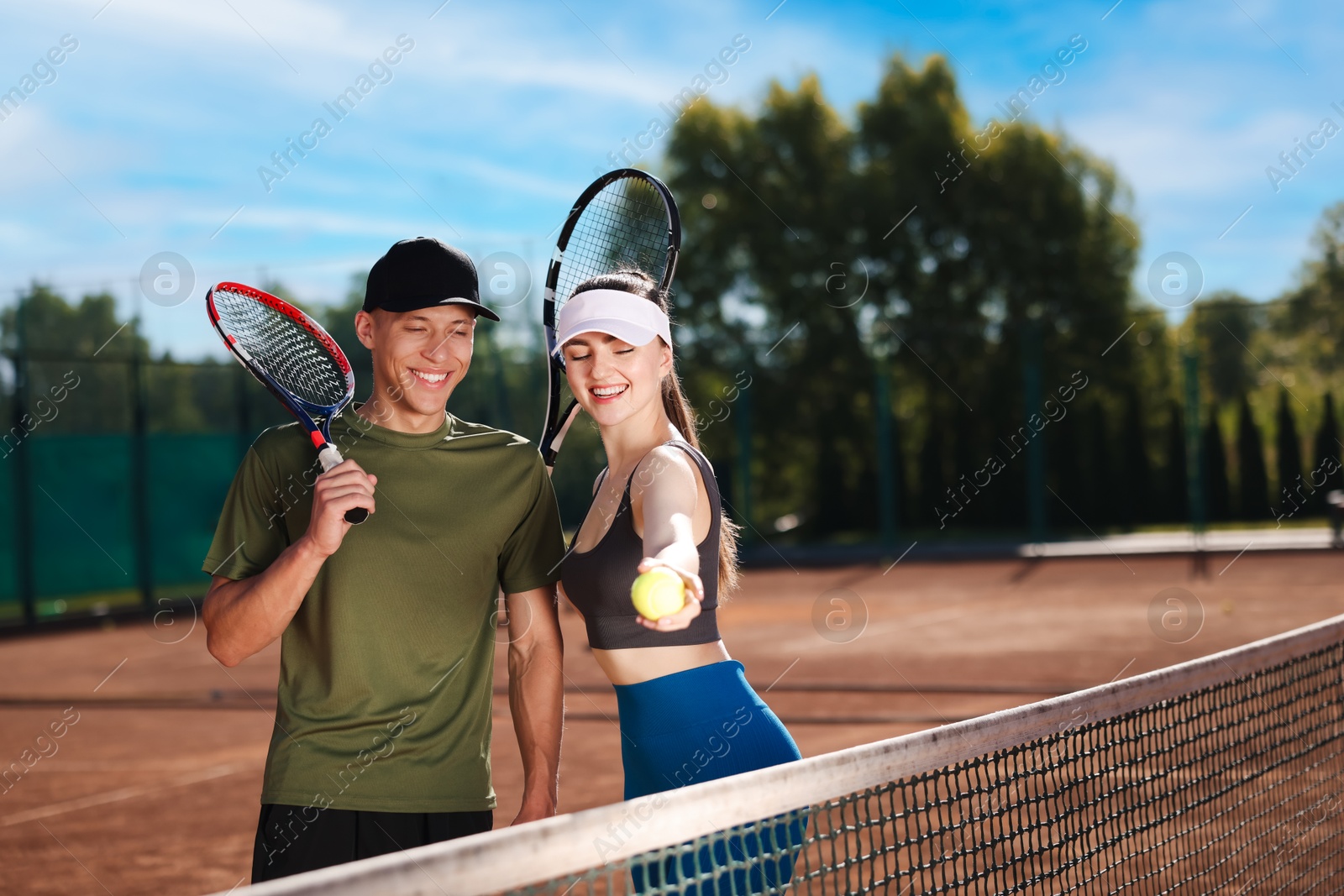 Happy couple with rackets and ball at tennis court. Space for text Photo of Happy couple with rackets and ball at tennis court. Space for text