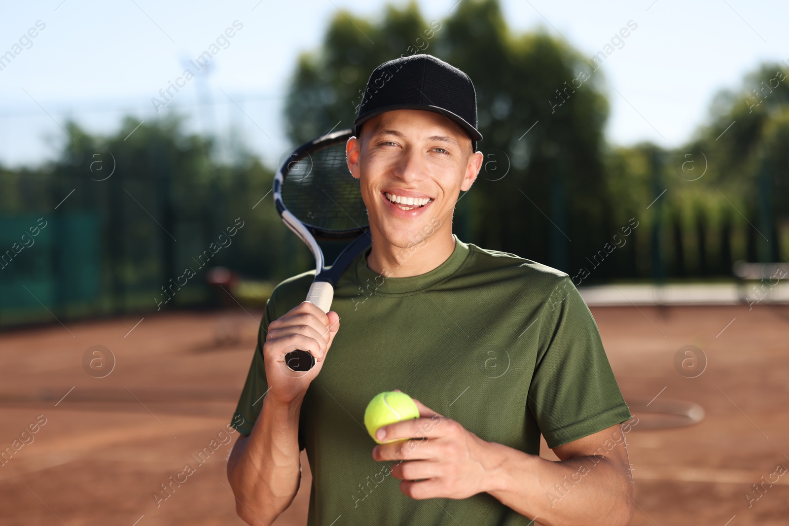 Smiling young man with racket and ball at tennis court Photo of Smiling young man with racket and ball at tennis court