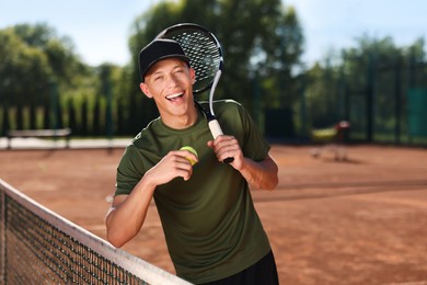 Photo of Smiling young man with racket and ball at tennis court