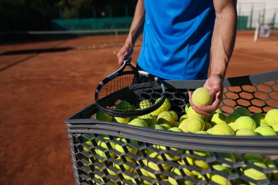 Photo of Man taking tennis ball out of cart at court, closeup