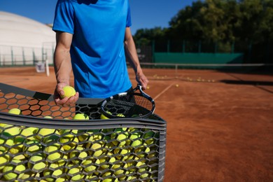 Photo of Man taking tennis ball out of cart at court, closeup