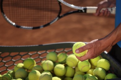 Photo of Man taking tennis ball out of cart at court, closeup