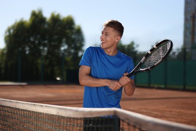 Photo of Young man with racket playing tennis at court. Space for text