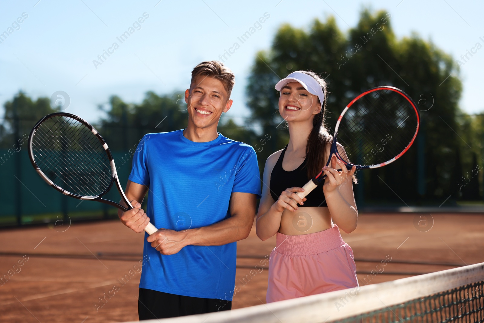 Happy man and woman with rackets at tennis court on sunny day Photo of Happy man and woman with rackets at tennis court on sunny day