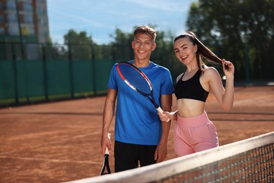 Photo of Happy man and woman with rackets at tennis court on sunny day