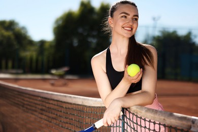 Photo of Happy woman with racket and ball at tennis court. Space for text