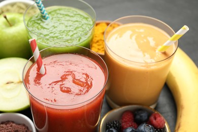 Photo of Superfood. Refreshing smoothies in glasses and ingredients on dark table, closeup