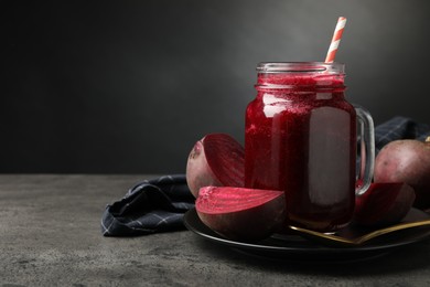 Photo of Superfood. Refreshing smoothie in mason jar and beetroot on grey textured table against dark background, closeup. Space for text