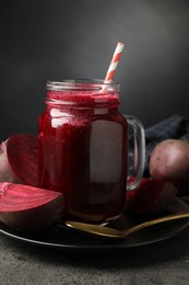 Photo of Superfood. Refreshing smoothie in mason jar and beetroot on grey textured table against dark background, closeup