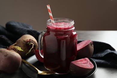 Photo of Superfood. Refreshing smoothie in mason jar and beetroots on grey textured table against brown background, closeup