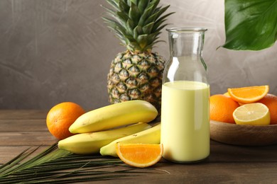 Photo of Superfood. Refreshing smoothie in bottle, palm leaf and ingredients on wooden table against grey background, closeup