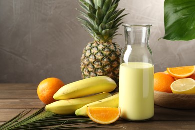 Photo of Superfood. Refreshing smoothie in bottle, palm leaf and ingredients on wooden table against grey background, closeup
