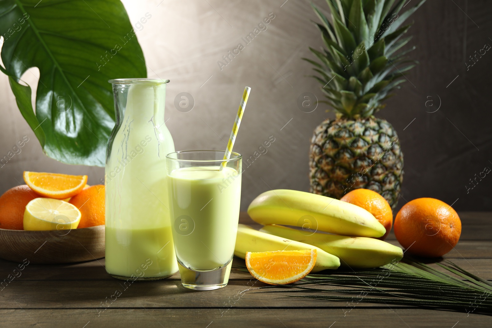 Superfood. Refreshing smoothie in bottle, glass, palm leaf and ingredients on wooden table against grey background Photo of Superfood. Refreshing smoothie in bottle, glass, palm leaf and ingredients on wooden table against grey background