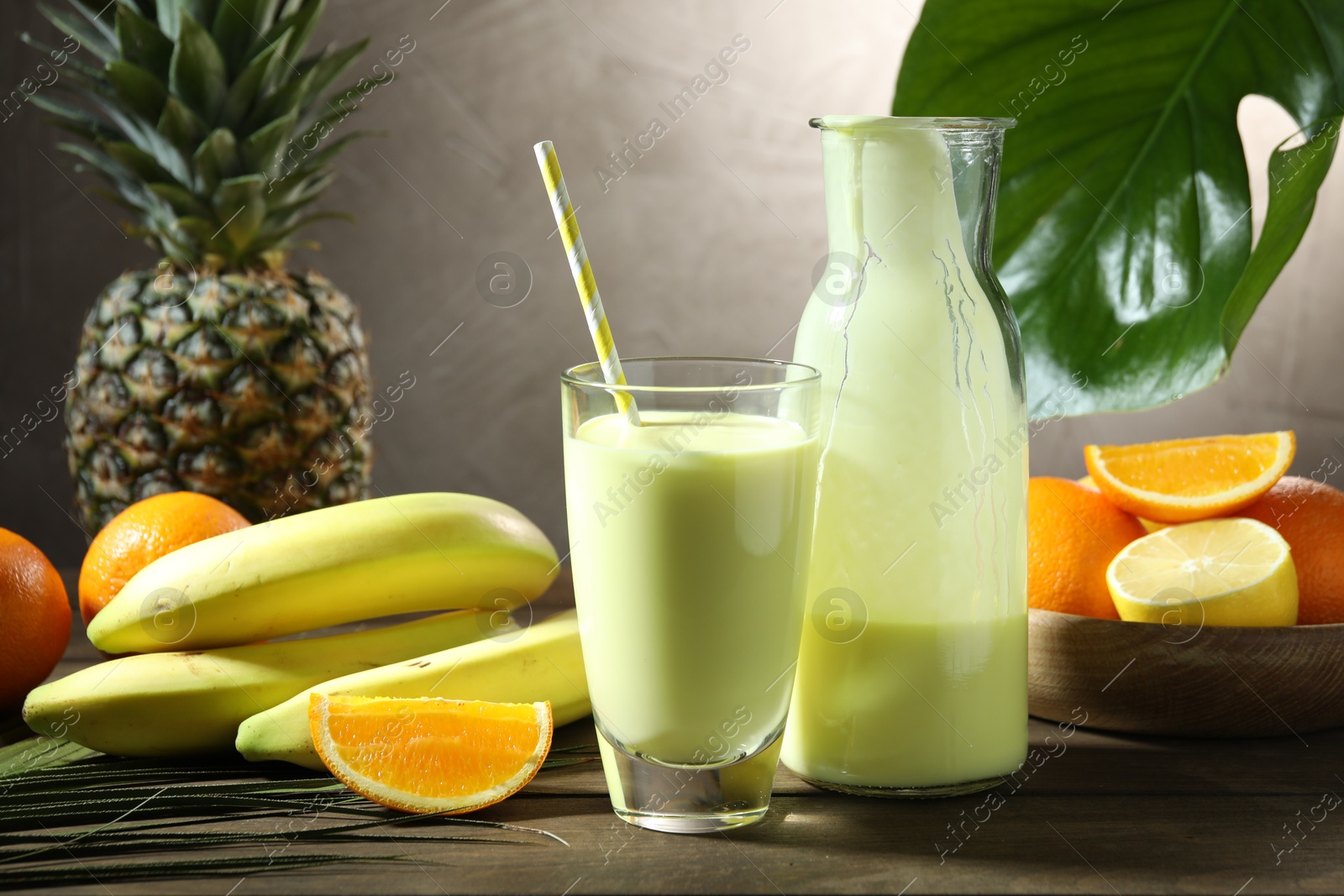 Superfood. Refreshing smoothie in bottle, glass, palm leaf and ingredients on wooden table against grey background Photo of Superfood. Refreshing smoothie in bottle, glass, palm leaf and ingredients on wooden table against grey background