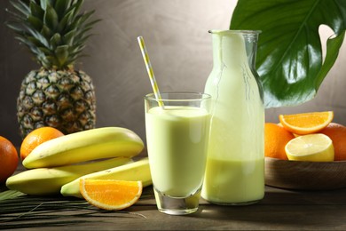 Photo of Superfood. Refreshing smoothie in bottle, glass, palm leaf and ingredients on wooden table against grey background