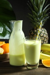 Photo of Superfood. Refreshing smoothie in bottle, glass and ingredients on wooden table against black background, closeup