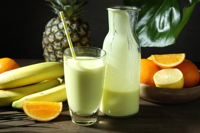 Photo of Superfood. Refreshing smoothie in bottle, glass and ingredients on wooden table against black background, closeup