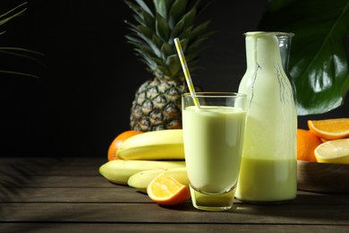 Photo of Superfood. Refreshing smoothie in bottle, glass and ingredients on wooden table against black background