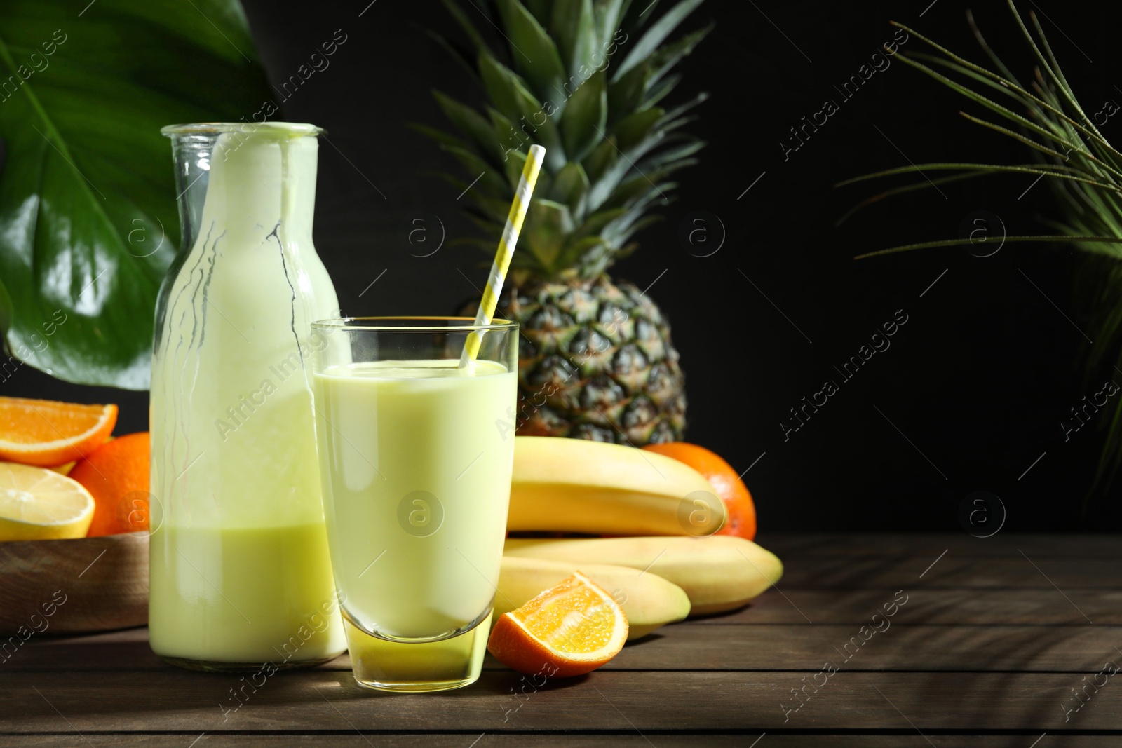 Photo of Superfood. Refreshing smoothie in bottle, glass and ingredients on wooden table against black background