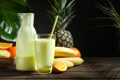 Photo of Superfood. Refreshing smoothie in bottle, glass and ingredients on wooden table against black background