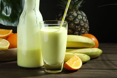 Photo of Superfood. Refreshing smoothie in bottle, glass and ingredients on wooden table against black background, closeup