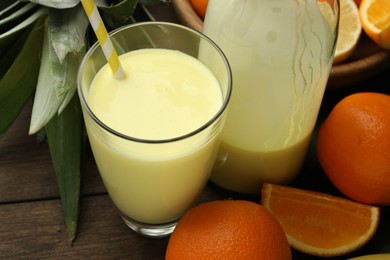 Photo of Superfood. Refreshing smoothie in glass, bottle, orange and leaves on wooden table, closeup