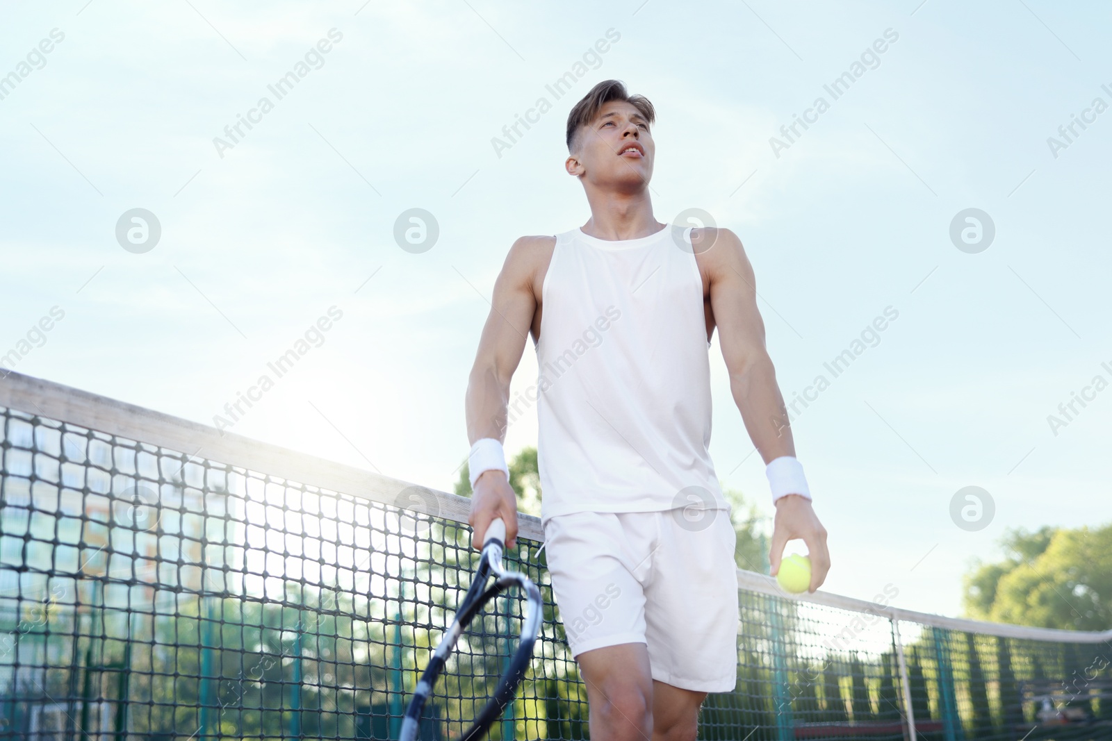 Young man playing tennis at court on sunny day, low angle view Photo of Young man playing tennis at court on sunny day, low angle view