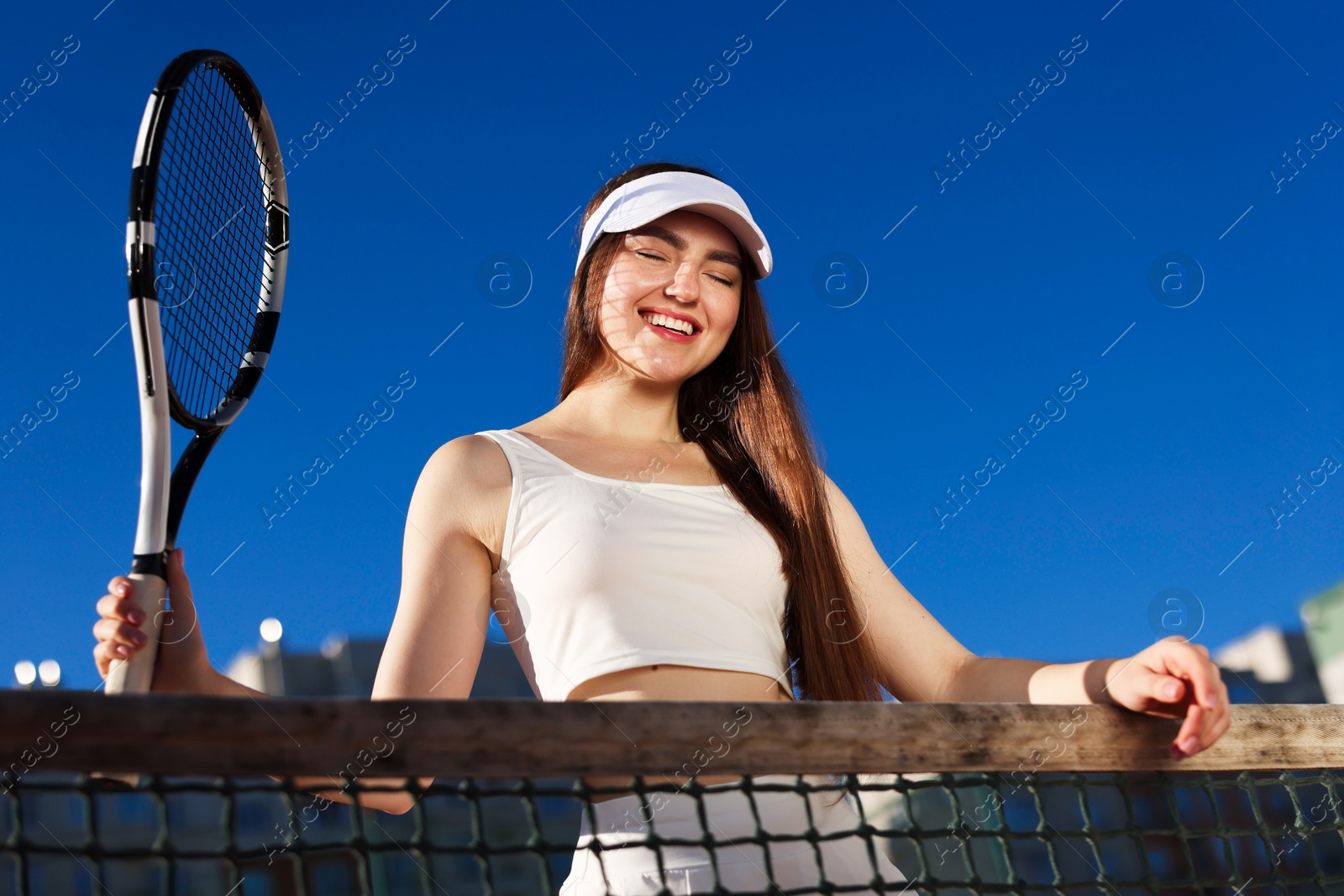 Beautiful woman with racket at tennis court, low angle view Photo of Beautiful woman with racket at tennis court, low angle view