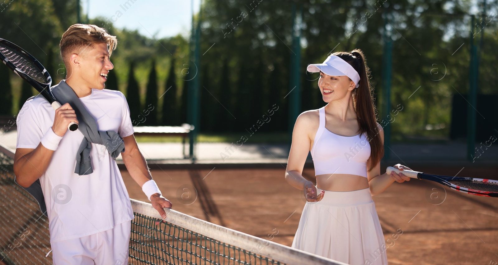 Happy woman and man with rackets at tennis court Photo of Happy woman and man with rackets at tennis court