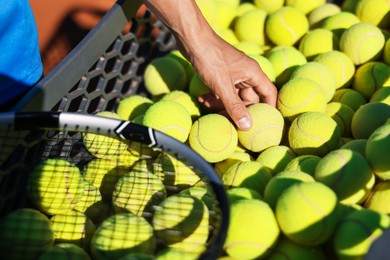 Photo of Man taking tennis ball out of cart at court, closeup