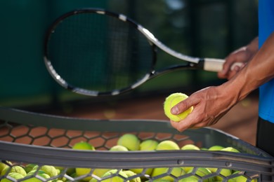 Photo of Man taking tennis ball out of cart at court, closeup