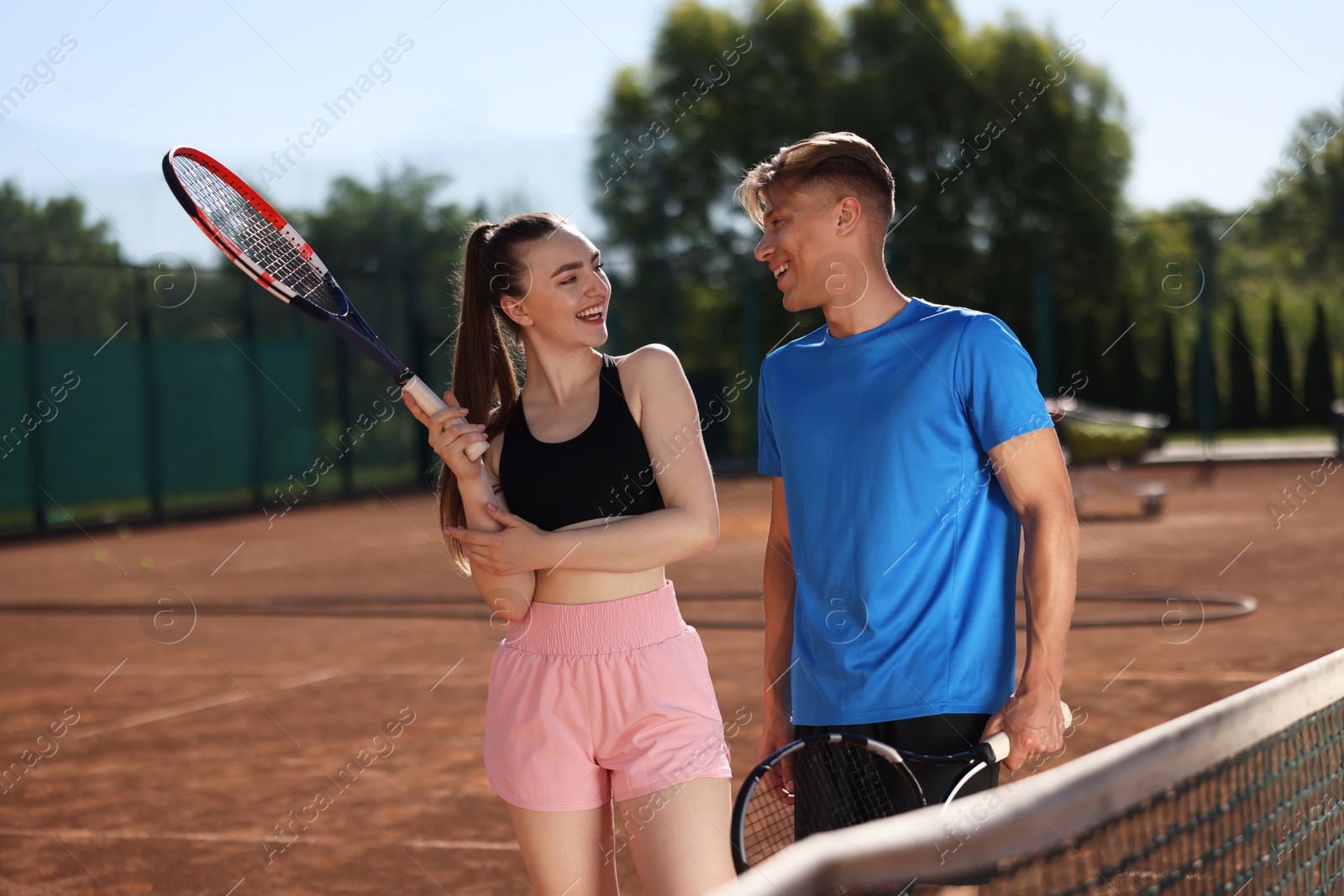 Happy man and woman with rackets at tennis court on sunny day Photo of Happy man and woman with rackets at tennis court on sunny day