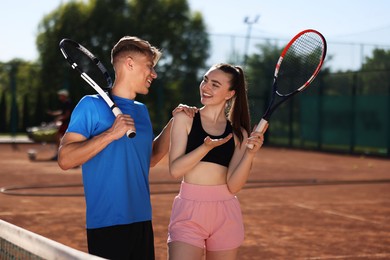 Photo of Happy man and woman with rackets at tennis court on sunny day