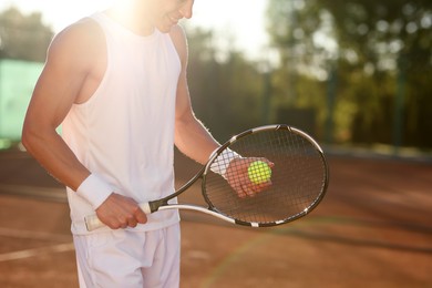 Photo of Man with tennis racket and ball at court on sunny day, closeup