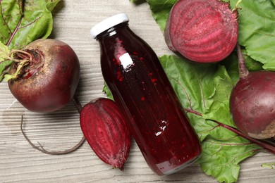 Photo of Superfood. Tasty juice in bottle and beetroots on light wooden table, flat lay