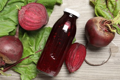 Photo of Superfood. Tasty juice in bottle and beetroots on light wooden table, flat lay