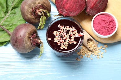 Photo of Superfood. Tasty juice with oats in glass, powder and beetroots on light blue wooden table, flat lay. Space for text