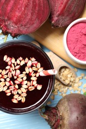 Photo of Superfood. Tasty juice with oats in glass, powder and beetroots on light blue wooden table, flat lay
