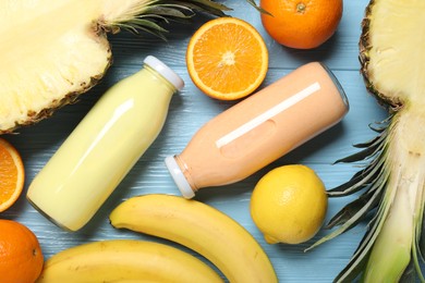 Photo of Superfood. Tasty smoothies in bottles and ingredients on light blue wooden table, flat lay