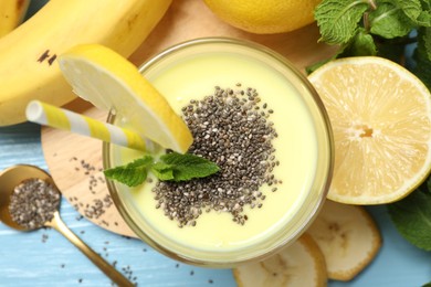 Photo of Superfood. Tasty smoothie with chia seeds in glass and ingredients on light blue wooden table, flat lay