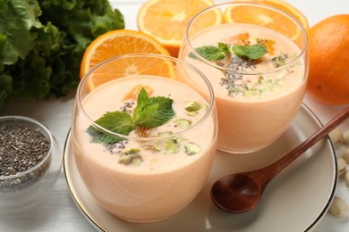 Photo of Superfood. Tasty smoothie with chia seeds, mint, pistachio and oranges on white wooden table, closeup