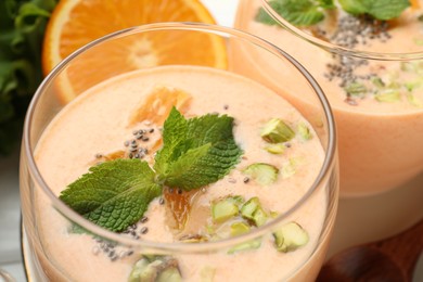 Photo of Superfood. Tasty smoothie with chia seeds, mint, pistachio and orange in glasses on white table, closeup