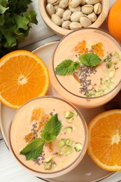 Photo of Superfood. Tasty smoothie with chia seeds, mint, pistachio and oranges on white wooden table, flat lay